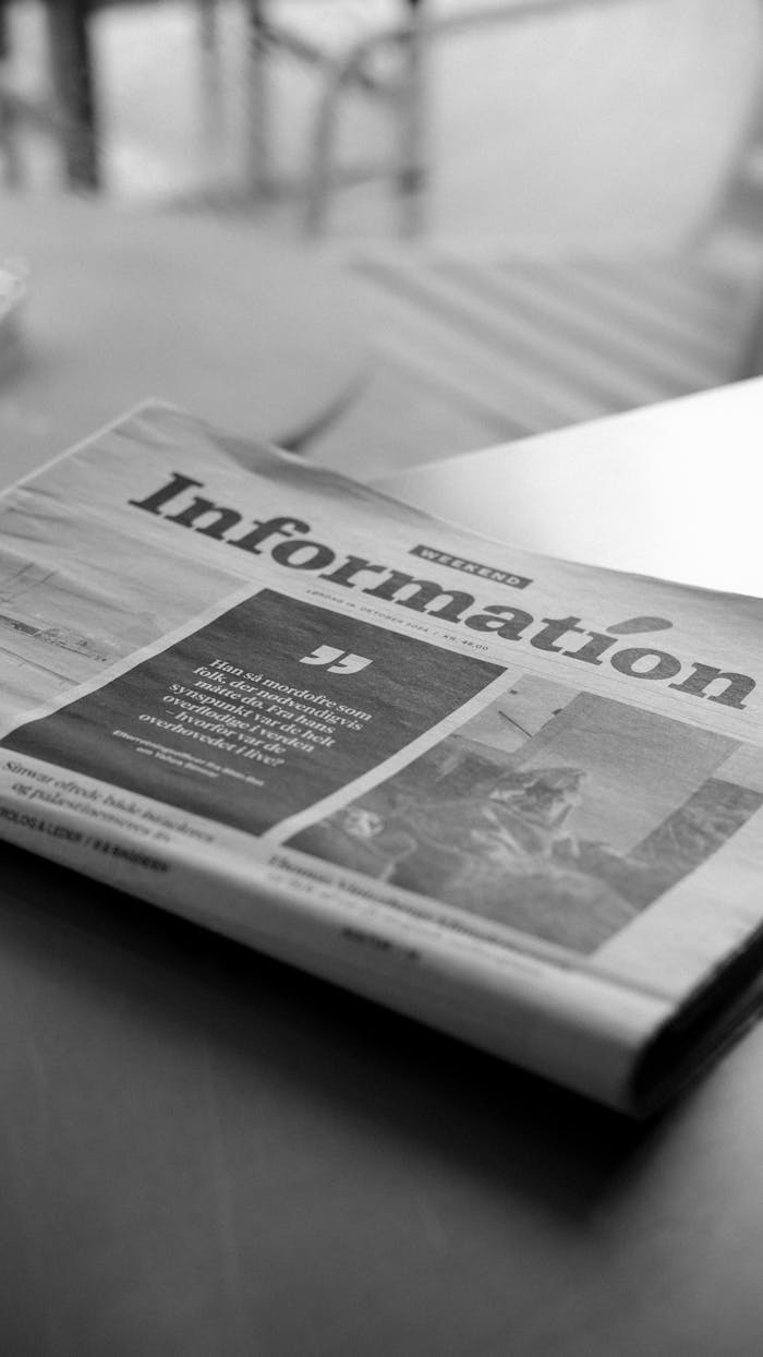 Monochrome image of a newspaper titled 'Information' in a cozy cafe setting.