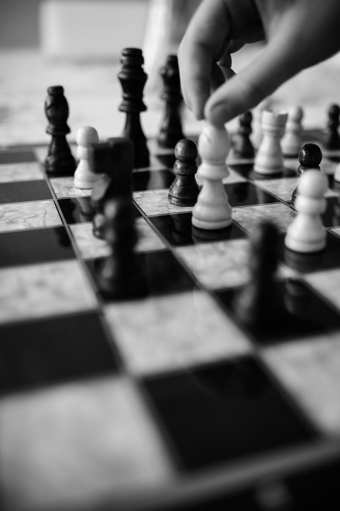 Black and white image of a hand moving chess pieces on a board, highlighting strategic play.
